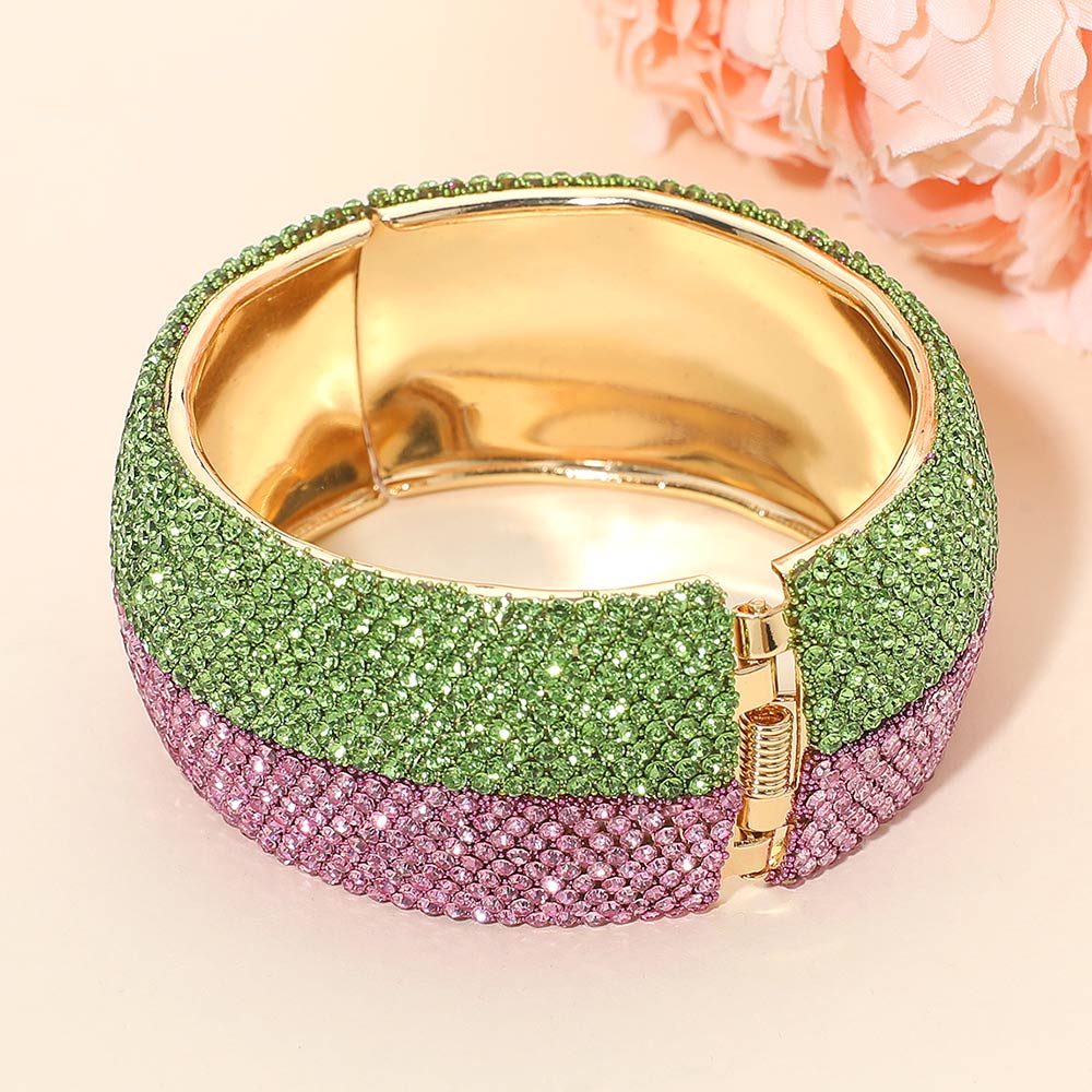 Gold bracelet with green and pink gemstones on a light background