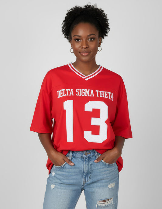 Person wearing a red 'Delta Sigma Theta 13' jersey with light blue jeans on a plain background