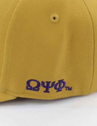 Close-up detail of purple Omega Psi Phi Greek letters embroidered on the side of a textured old gold baseball cap.
