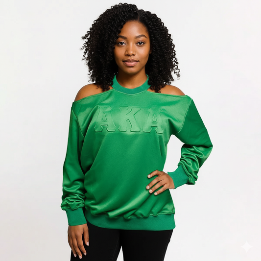 Black woman modeling a vibrant green satin AKA cold-shoulder sweatshirt with embossed letters and a mock neck, paired with black pants.