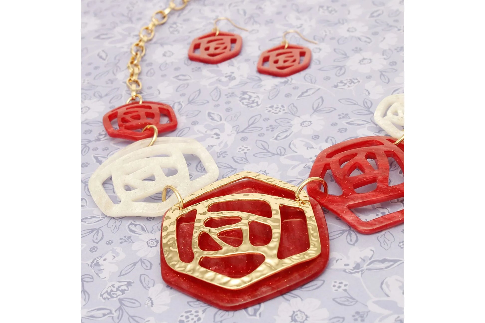 Jewelry set with red and gold necklace and earrings on a light gray background