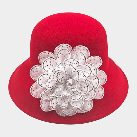 A red felt hat with a large white flower adorned with rhinestones.